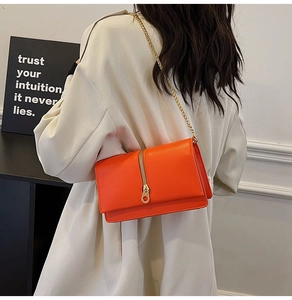Detail of orange textured leather crossbody bag with gold chain strap and zipper accent