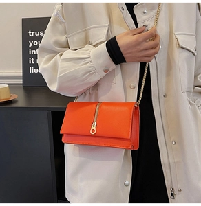 Detail of bright orange crossbody bag with gold vertical zipper and metal chain strap