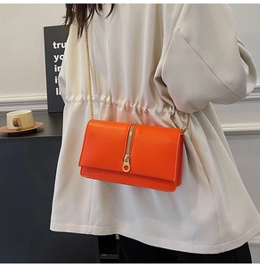 Detail of orange minimalist crossbody bag featuring gold zipper and metal chain strap