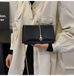 Detail of a black textured crossbody bag with gold chain strap worn with a beige blazer