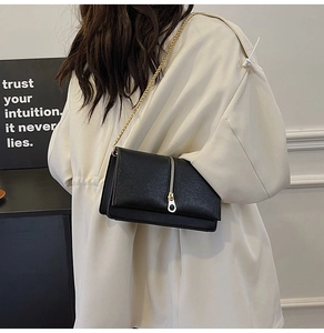 Detail of black pebbled leather crossbody bag with gold chain strap on model