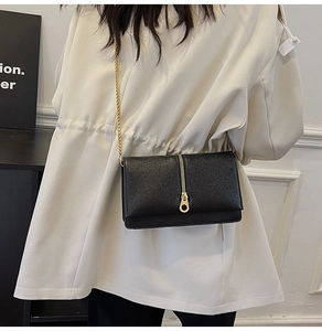 Close-up of a black cross-grain leather bag with gold ring zipper and chain strap detail