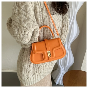 Gros plan du sac bandoulière orange vif avec fermoir tournant doré sur une tenue minimaliste