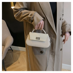 Detail of cream crossbody bag with silver metal turn-lock and chain strap on trench coat