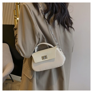 Detail of a chic cream crossbody bag with silver chain and metal lock worn with a blazer