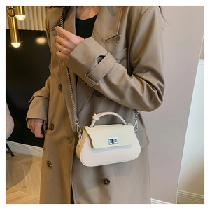 Detail of cream crossbody bag with silver twist lock and knot handle on trench coat