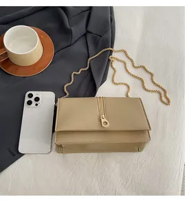 Detailed size comparison of khaki crossbody bag with chain strap against a smartphone