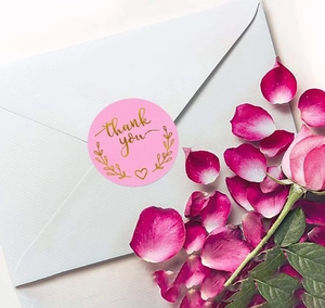 Pink round thank you stickers with gold foil lettering on a white envelope with roses