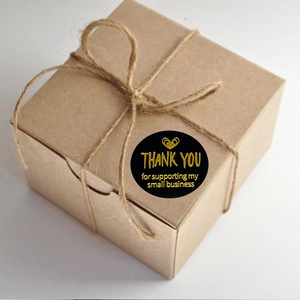 Black round Thank You stickers with gold lettering on brown kraft gift box decoration