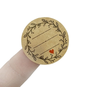 Kraft paper round label with olive branch and red heart held by fingers for size