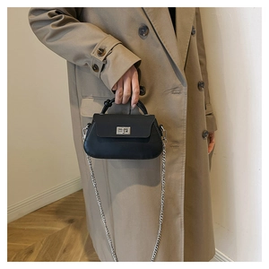 Detail of a black mini crossbody bag with silver twist lock on a beige trench coat