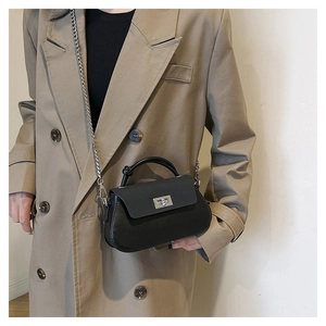Close-up of black crossbody bag with silver twist lock and chain on khaki coat