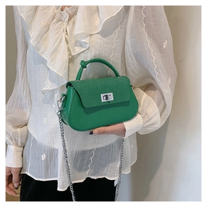 Detail view of green patchwork crossbody bag with silver twist lock on white lace shirt