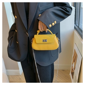 Detail of yellow crossbody bag featuring a silver metal turn-lock and chain strap