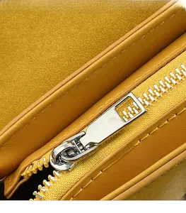 Detail of silver metallic zipper pull and matte yellow suede texture on women's handbag