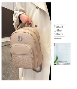 Close-up of beige quilted faux leather backpack featuring circular metal logo and zip detail