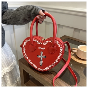 Detail of red heart-shaped punk crossbody bag with cross pattern and baby print on table
