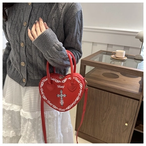 Detail of red heart-shaped leather bag with gothic cross and flame print in home setting