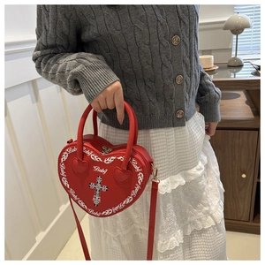 Detail of red heart-shaped punk crossbody bag with cross emblem and baby flame graphics