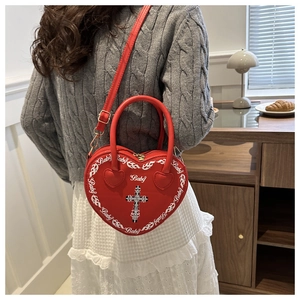 Close-up of red heart-shaped bag with white baby text and cross detail in a cozy setting