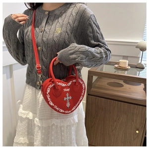 Macro detail of red heart-shaped punk crossbody bag with cross print and stud accents