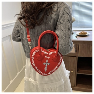 Red heart-shaped bag with Baby print and cross detail carried by a model in casual setting