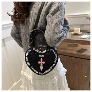 Detail of a black heart-shaped handbag with gothic cross and baby prints shown on a model