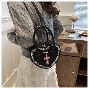 Detail of heart-shaped punk bag with Baby text and cross prints shown on shoulder