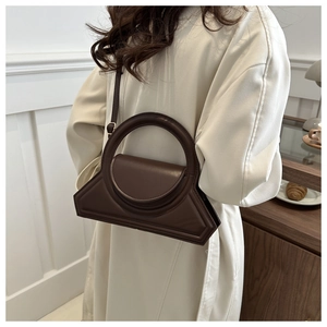 Detail of dark brown leather handbag with unique circular handle and trapezoid structure
