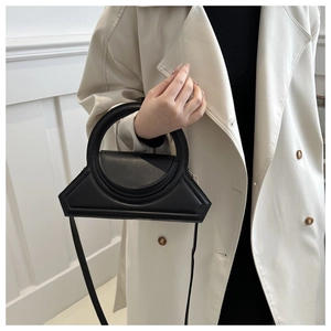 Detail of a black geometric handbag with a round handle and matte faux leather texture