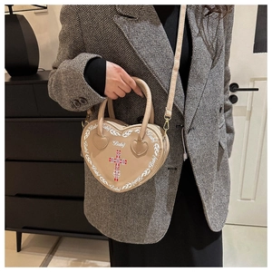 Detail showing beige heart-shaped bag with red cross pattern and top handle design