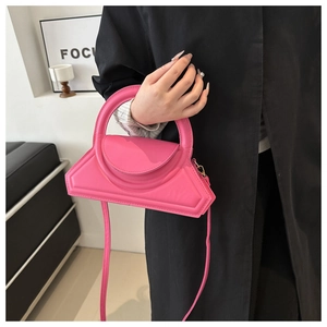Detail of a bright fuchsia geometric handbag held by a model in a black coat