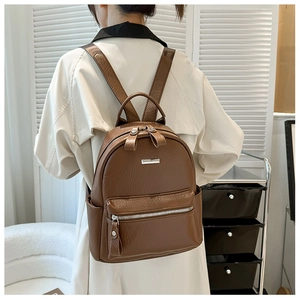 Side view of a soft brown leather backpack with silver metal bar detail on a female model