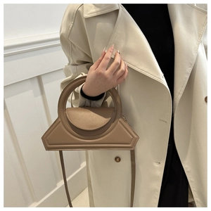 Niche khaki geometric handbag with large round handle shown on a beige trench coat