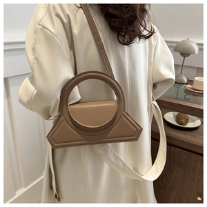 Lifestyle shot of a khaki geometric handbag with a round handle on a cafe table