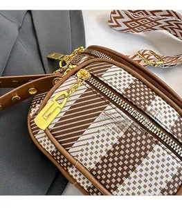 Detail of crossbody bag showing multi-layer zippers and geometric patterned wide strap