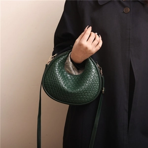 Green woven crescent shoulder bag with gold hardware worn by model in black coat