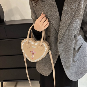 Beige heart-shaped crossbody bag with gothic cross and flame graphics worn by model