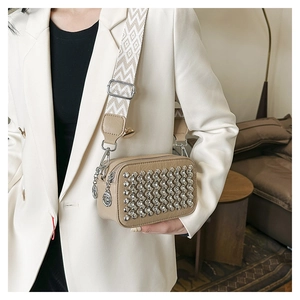 Beige camera bag with silver studs and wide geometric strap worn on a white blazer