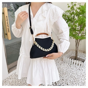 Detail of black textured fabric handbag featuring wood handle and chunky gold chain
