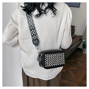 Detail of black crossbody bag with silver studs and wide geometric patterned strap