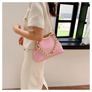Detailed view of pink woven crossbody bag with gold chain strap on a model's shoulder