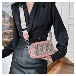 Close-up of pink crossbody bag with silver studs and patterned wide strap detail