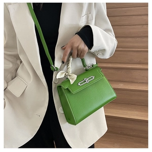 Detail einer grünen Kelly-Tasche mit Silberverschluss und Seidenschal auf Holzstufen