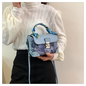 Close-up of vintage embroidered box bag with scarf-wrapped handle and metal lock detail