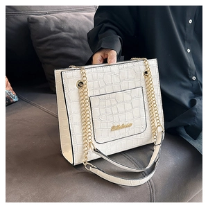 Vue détaillée du sac blanc avec motif crocodile et chaîne dorée sur un canapé sombre