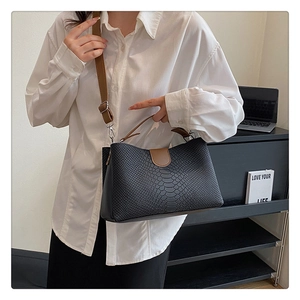 Close-up of black crocodile pattern PU leather bag with contrasting brown shoulder strap