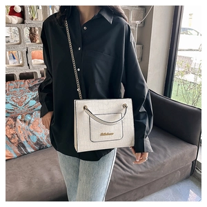 Détail du sac cabas blanc à motif crocodile avec chaîne dorée et plaque logo à l'épaule