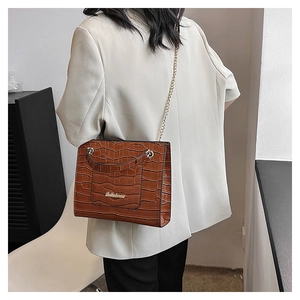 Détail d'un sac à main marron texture crocodile avec chaîne dorée porté par un mannequin