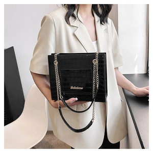 Gros plan sur un sac cabas noir motif croco avec chaîne dorée sur costume beige